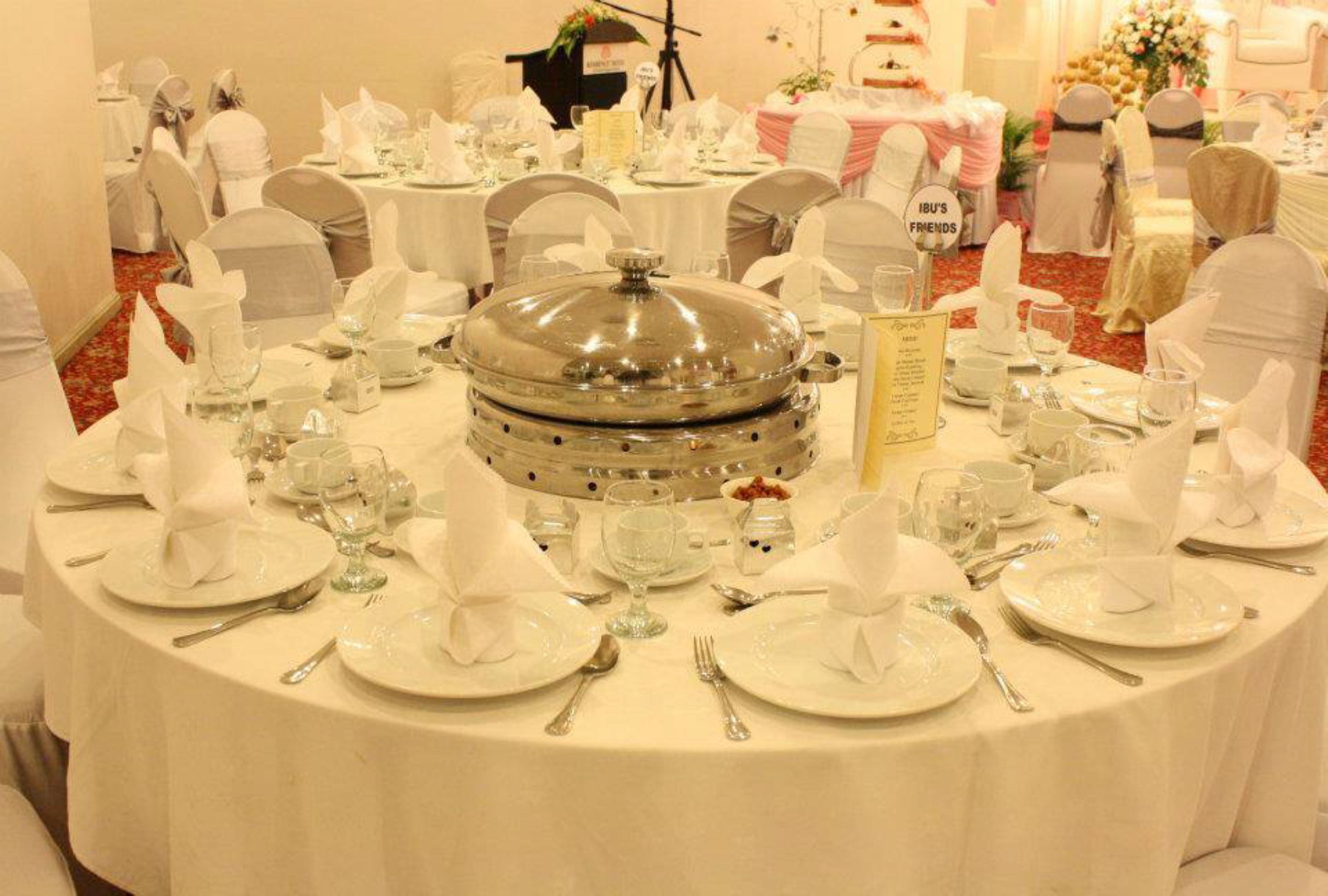 A banquet hall with round tables set for a formal event, complete with white tablecloths, glassware, and silverware.