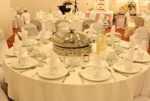 A banquet hall with round tables set for a formal event, complete with white tablecloths, glassware, and silverware.