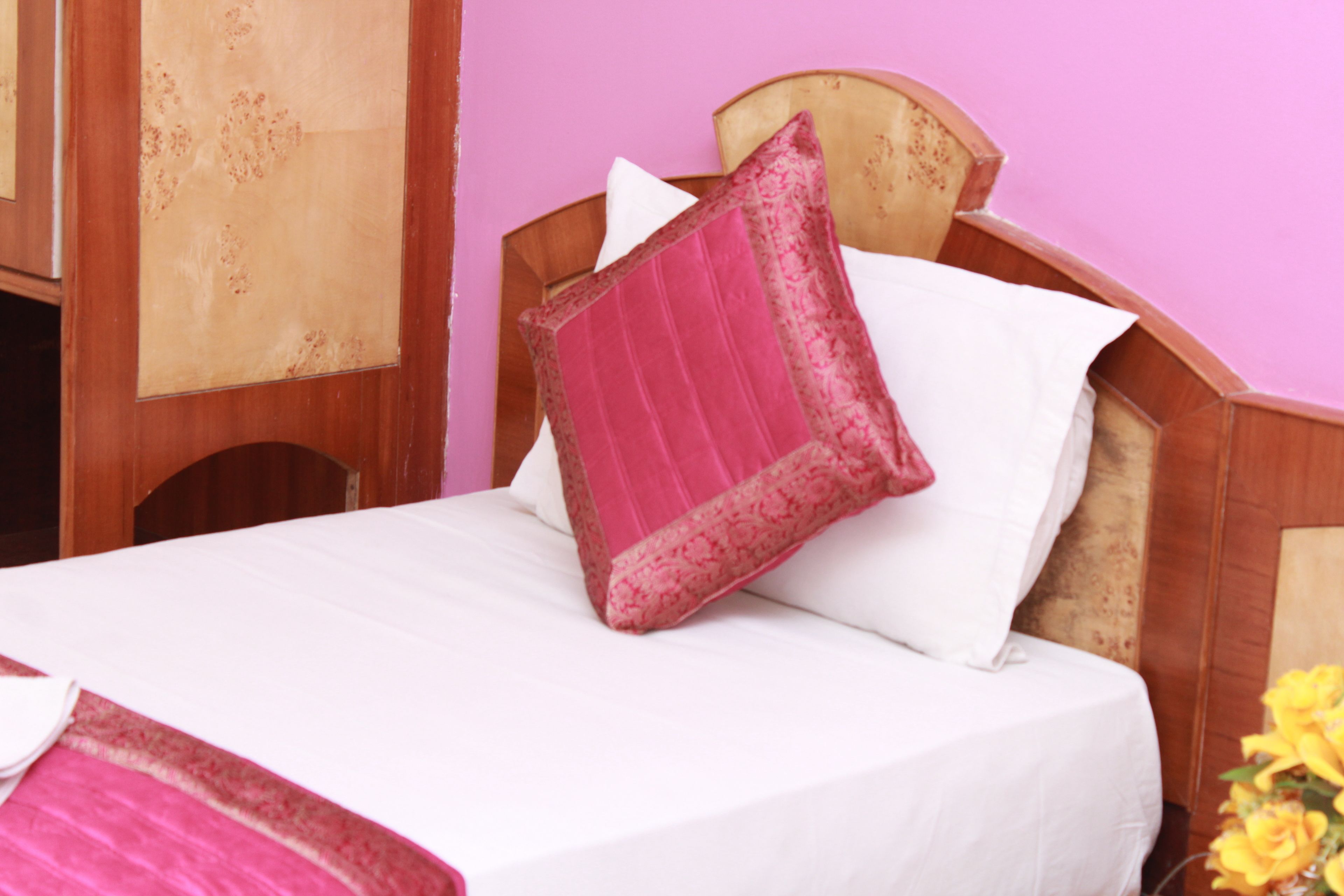 Un lit avec une tête de lit en bois, une literie blanche et un oreiller rose.