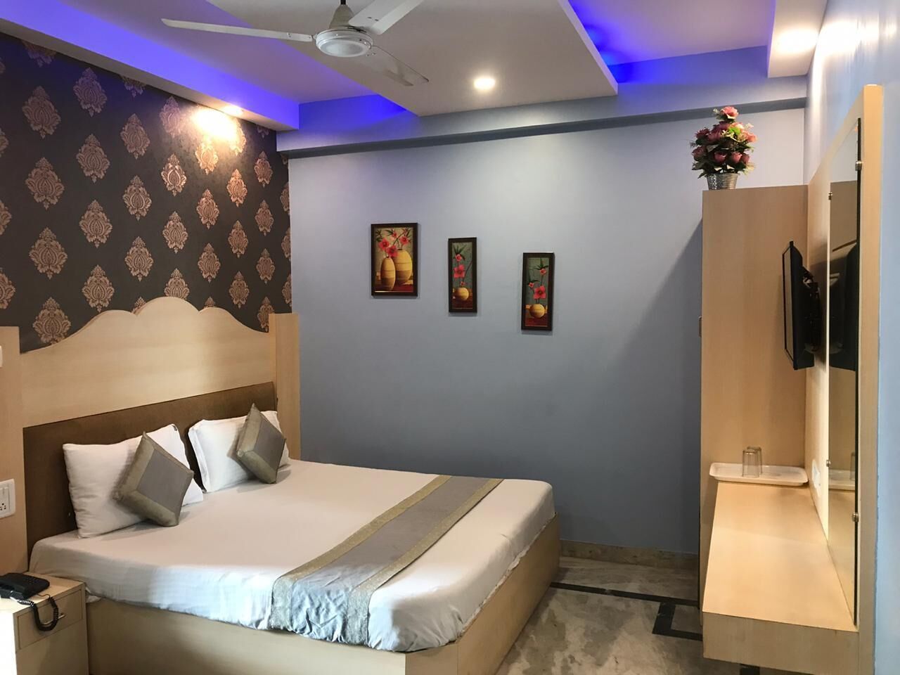 A hotel room with a bed, a nightstand, a TV, and a small table with a vase of flowers.