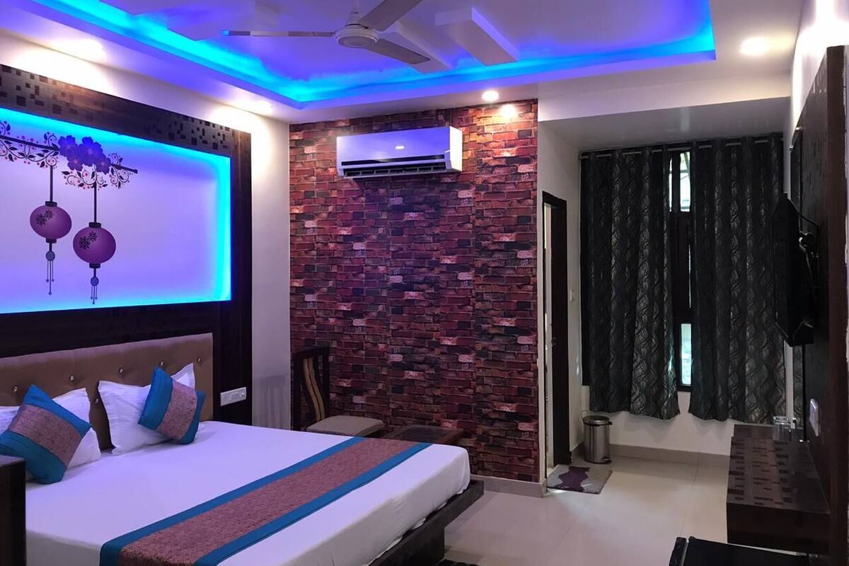 A modern bedroom with a brick-patterned accent wall, a bed with a blue and white bedspread, a ceiling fan, and an air conditioning unit.