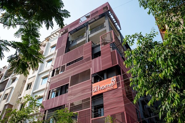 A multi-story building with a modern architectural design, featuring balconies and a prominent signage for 'At Home Suites'.