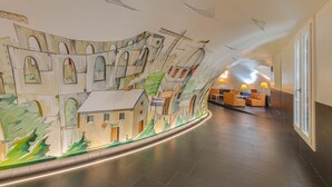 A spacious lobby with a mural of a building and construction cranes, a curved seating area, and a modern design. - Trevi Palace Hotel (Rome)
