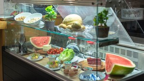 A display case with various food items including a watermelon, cheese, and other snacks. - Trevi Palace Hotel (Rome)