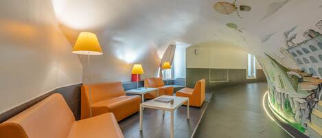 A modern lounge area with orange seating, a white table, and a mural on the wall.