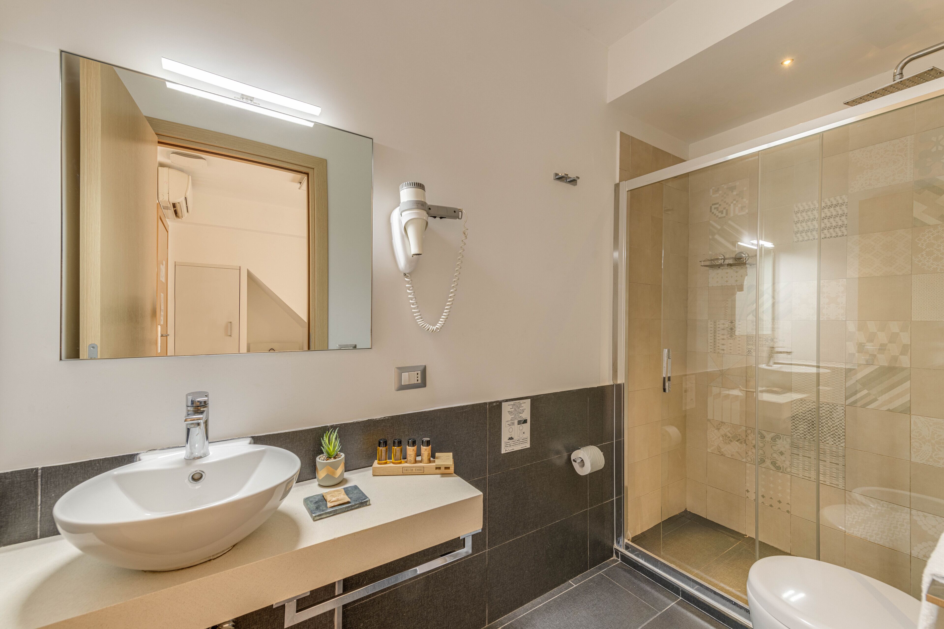 Un bagno moderno con un lavandino ampio, uno specchio, un asciugacapelli montato a parete e un box doccia in vetro.
