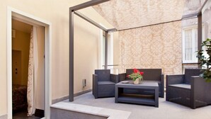 A modern outdoor seating area with wicker furniture and a small table with a vase of flowers. - Trevi Palace Hotel (Rome)