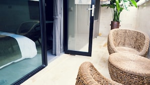 A hotel room with a bed, a wicker chair, a potted plant, and a sliding glass door. - Busan Amare Hotel (Busan)