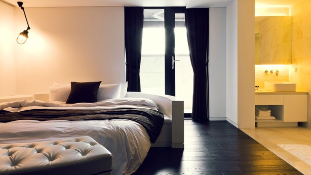 A modern bedroom with a large bed, a bedside table, a nightstand, and a bathroom with a sink and mirror. - Busan Amare Hotel (Busan)