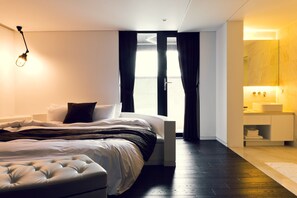 A modern bedroom with a large bed, a bedside table, a nightstand, and a bathroom with a sink and mirror. - Busan Amare Hotel (Busan)