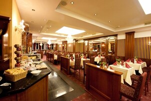 Un amplio comedor de hotel con varias mesas y sillas, una barra de buffet y una gran lámpara de araña.