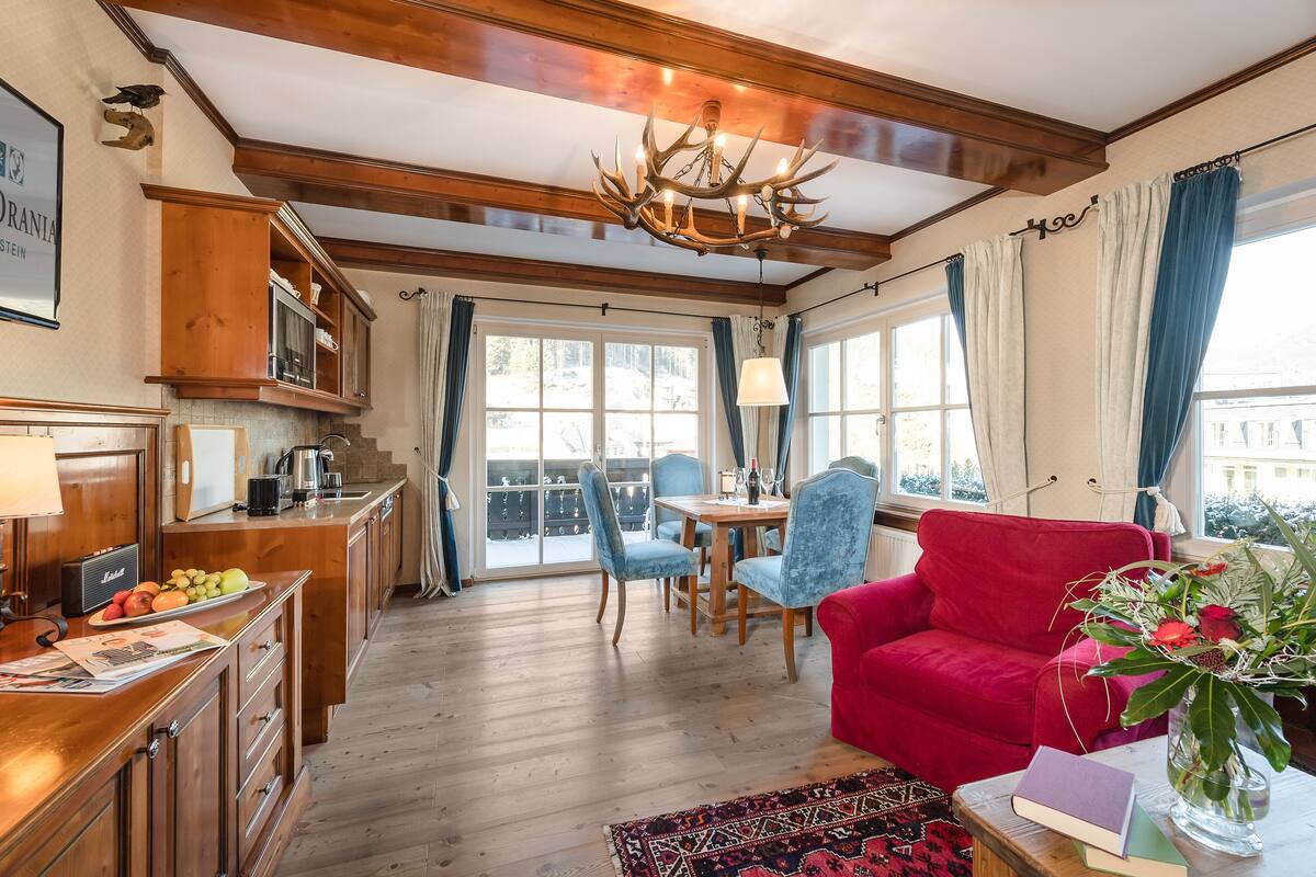 A cozy living room with a red sofa, a dining table with chairs, and a chandelier.