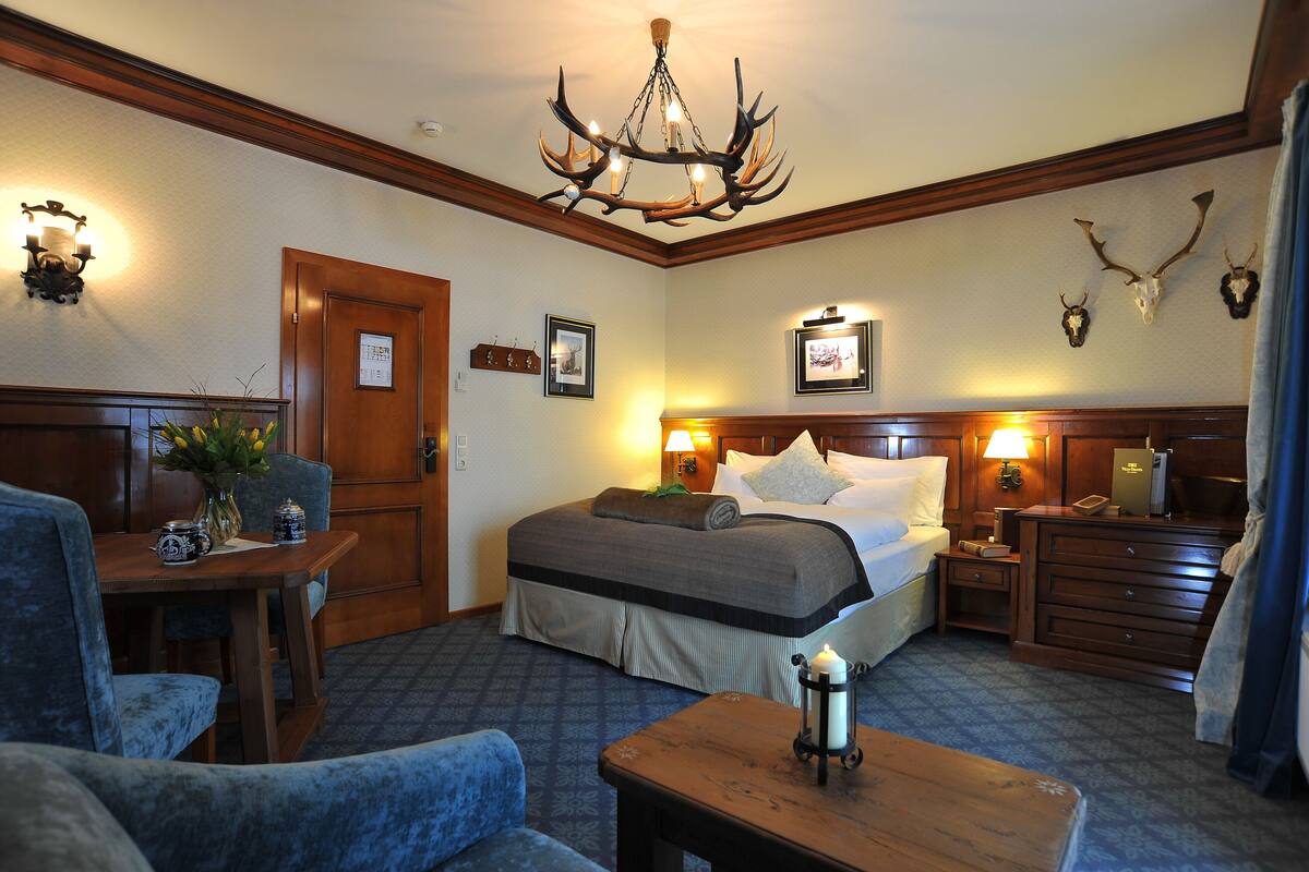 A hotel room with a large bed, a wooden headboard, a chandelier, and wall-mounted deer antlers.