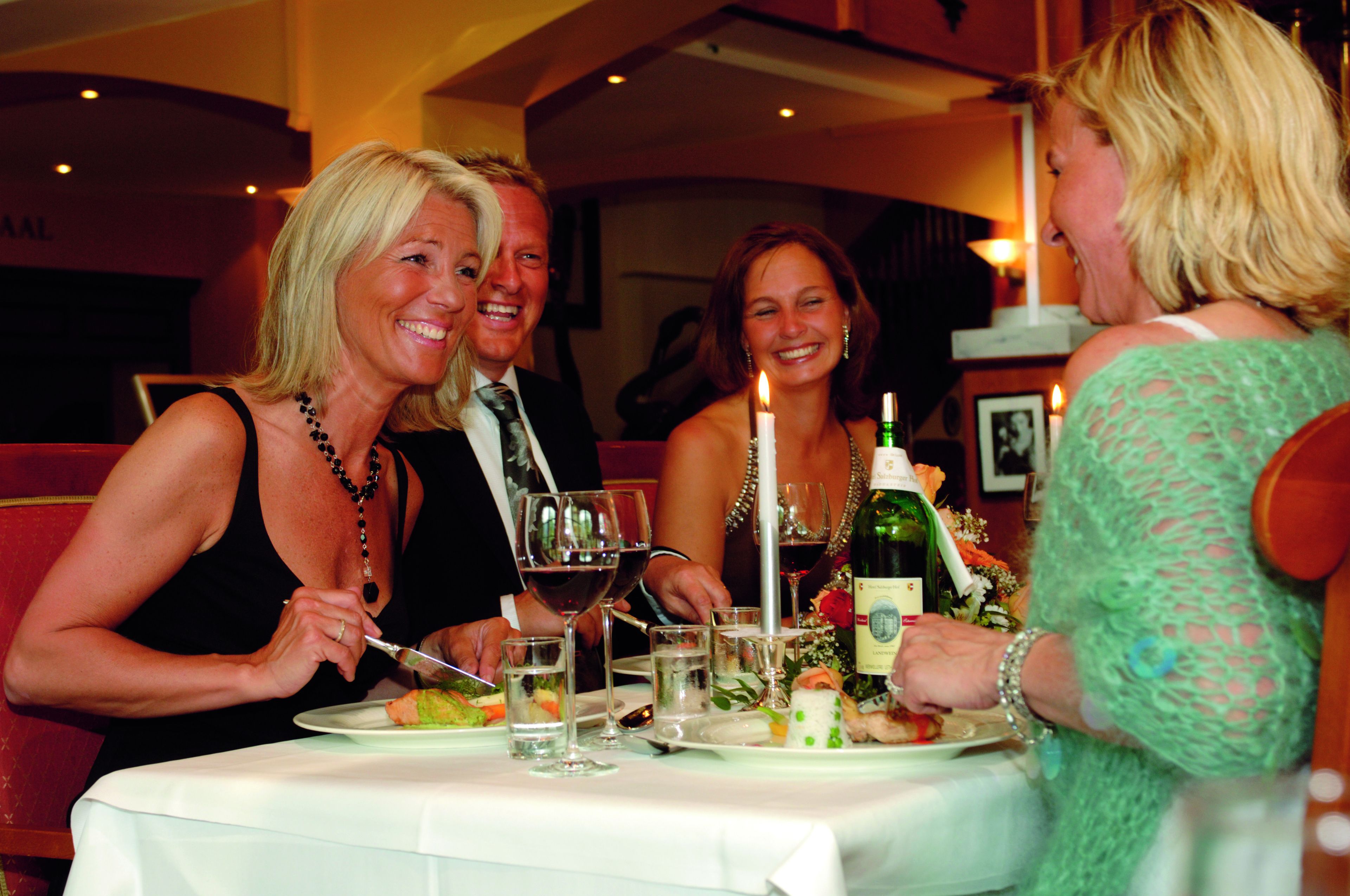 A group of people dining at a restaurant with a table set for a meal, wine glasses, and a candle.