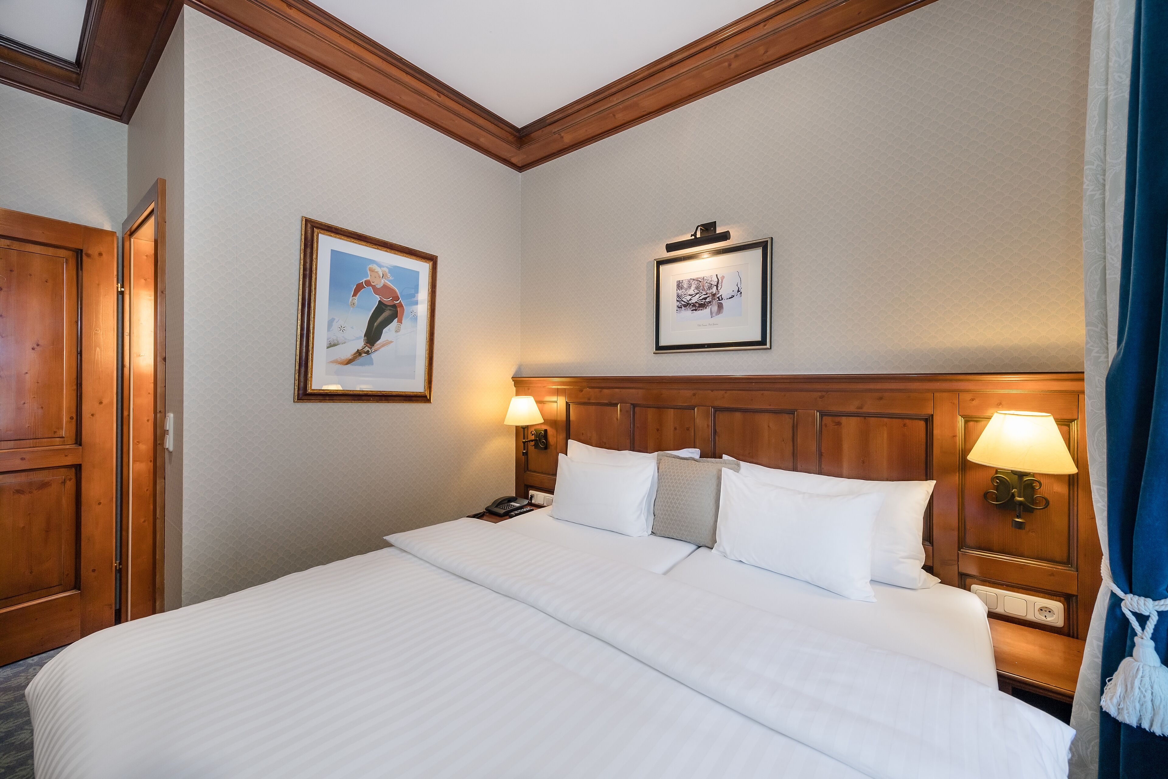 A hotel room with a large bed, wooden headboard, two bedside lamps, and framed pictures on the walls.