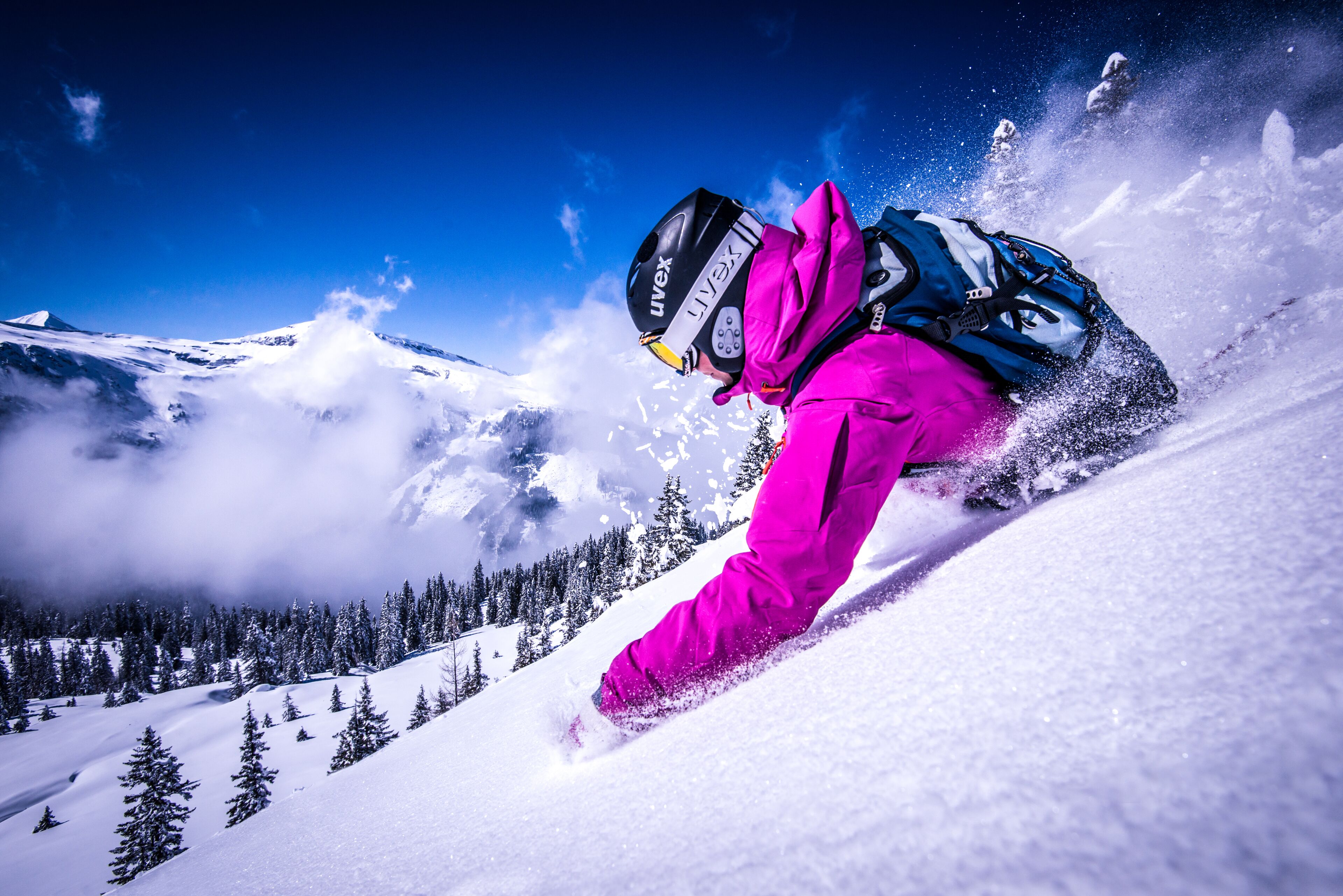 A person skiing down a snowy slope with a clear blue sky and mountains in the background.