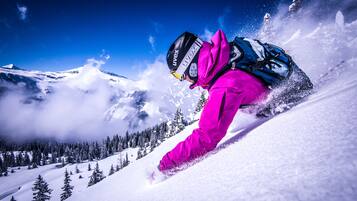 A person skiing down a snowy slope with a clear blue sky and mountains in the background.