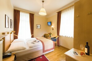A hotel room with a bed, a desk with a wine bottle, a chair, a TV, and a telephone. - Hotel Gisela (Bad Gastein)