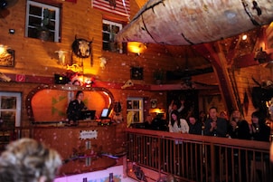 Interior de madera con un escenario, público y diversas decoraciones.