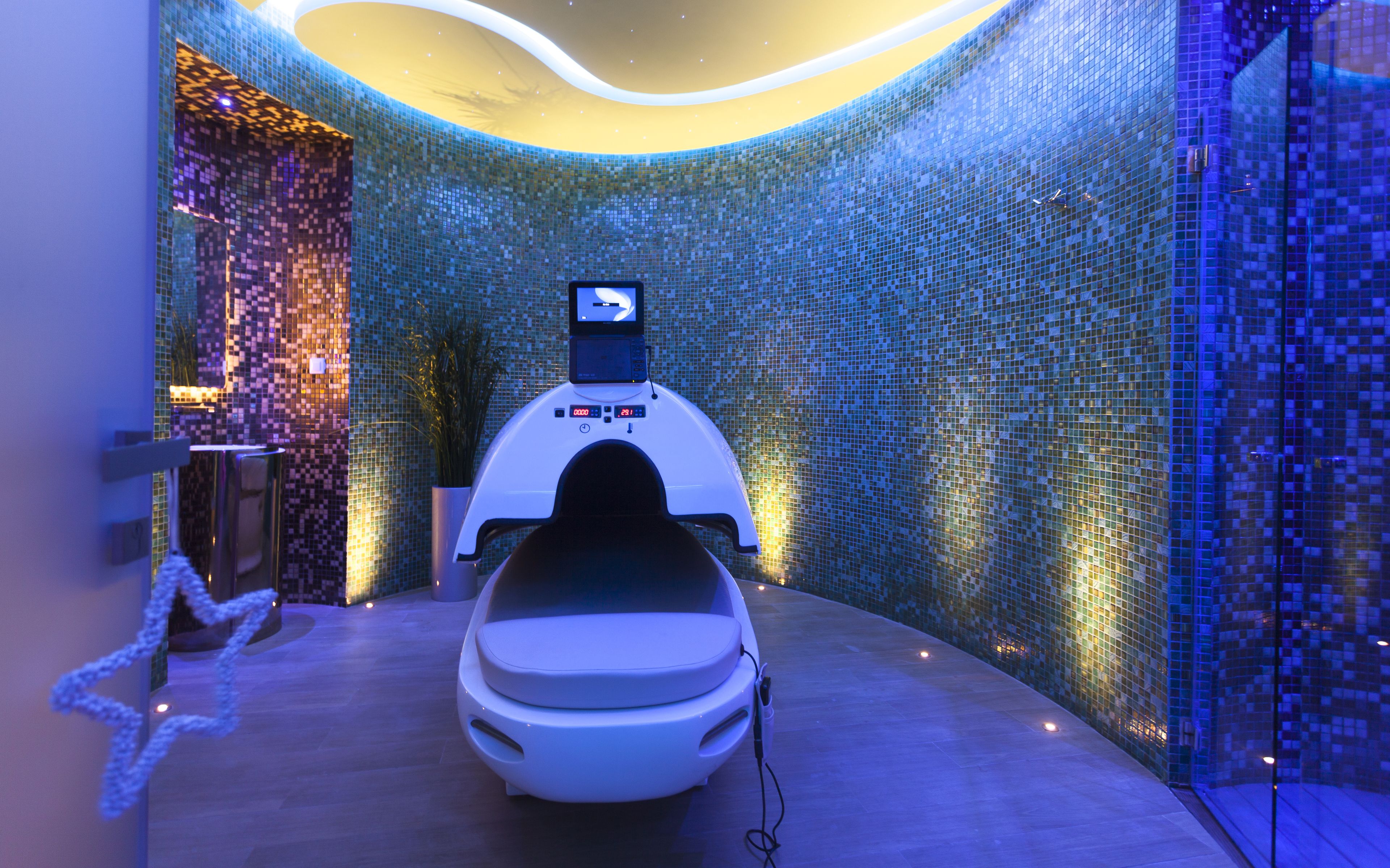 A modern spa room with a massage chair, a digital display, and mosaic walls.