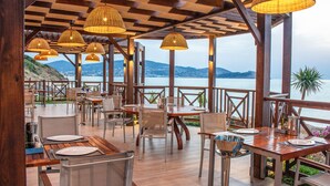 An outdoor dining area with wooden tables and chairs, wicker lamps, and a view of the sea. - La Cigale Tabarka Hôtel Spa & Golf (Tabarka)