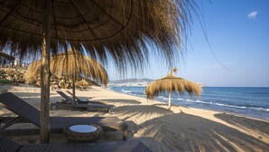 A beach with thatched umbrellas, lounge chairs, and a wicker table. - La Cigale Tabarka Hôtel Spa & Golf (Tabarka)