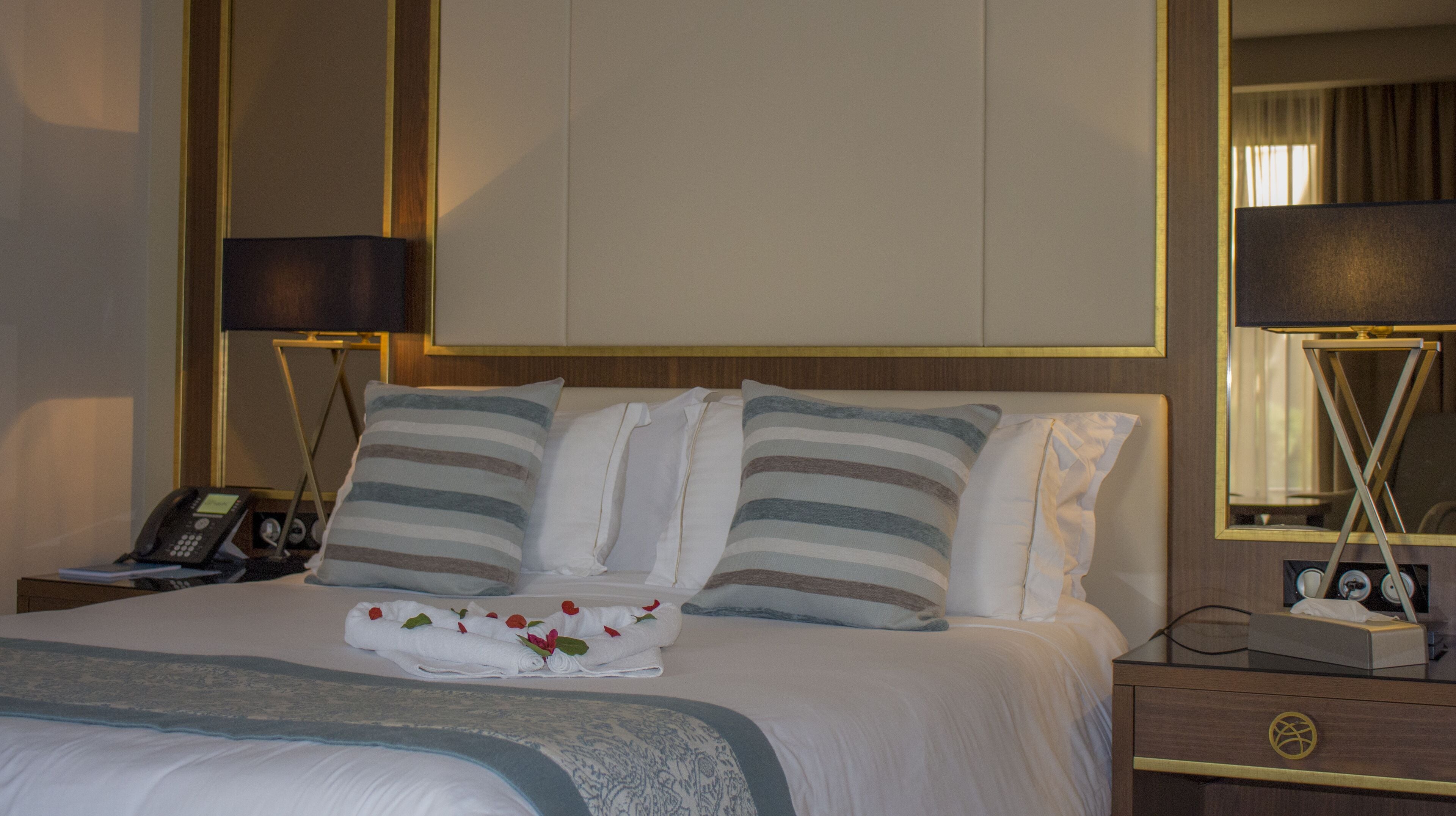 Une chambre d’hôtel avec un lit bien fait, un téléphone sur la table de chevet et une petite table de nuit avec une lampe et un cadre photo.