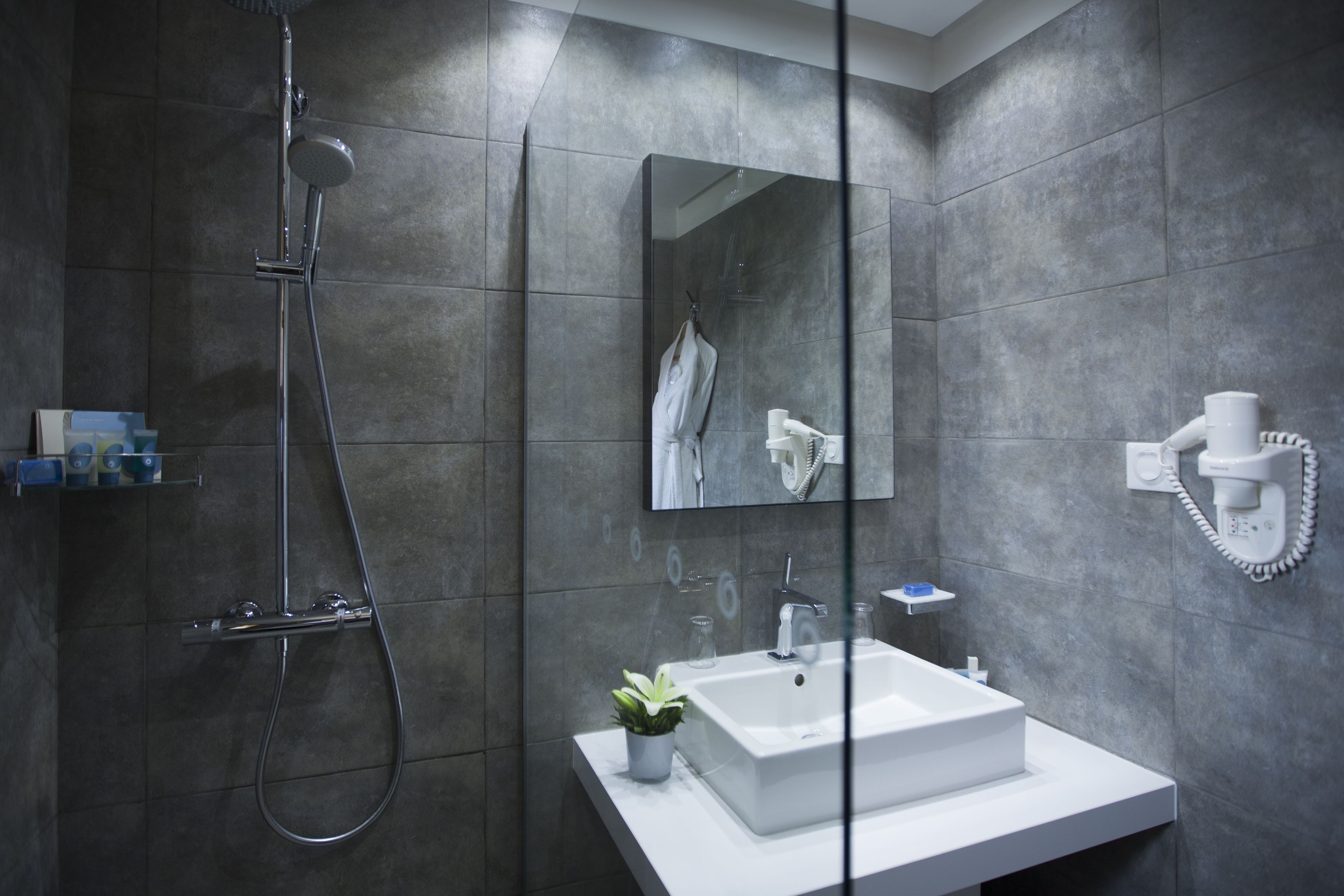 A modern bathroom with a large mirror, a white sink, and a handheld showerhead.