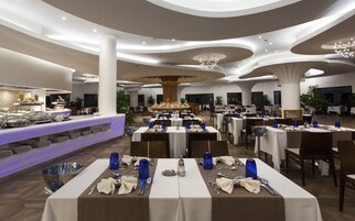 A modern restaurant with round tables, white tablecloths, and blue glassware.