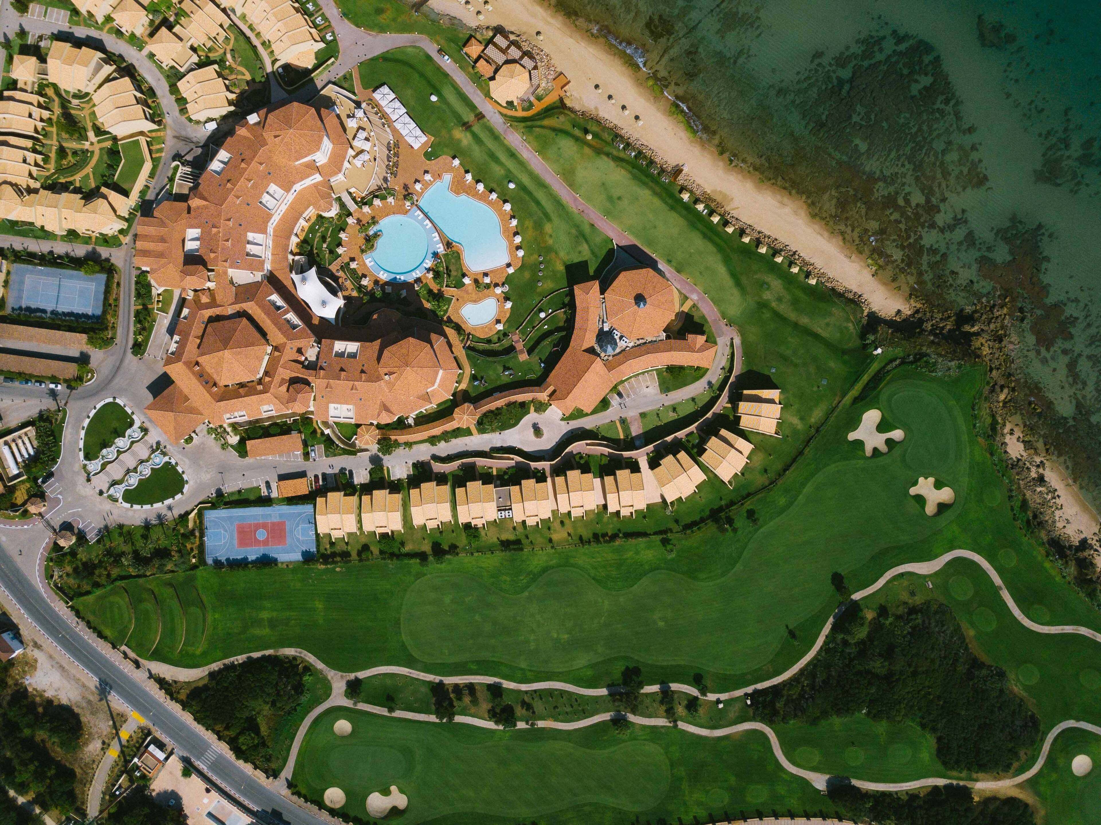 An aerial view of a resort with multiple buildings, a large central pool, and well-maintained golf courses.