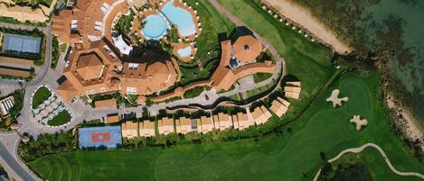 An aerial view of a resort with multiple buildings, a large central pool, and well-maintained golf courses.