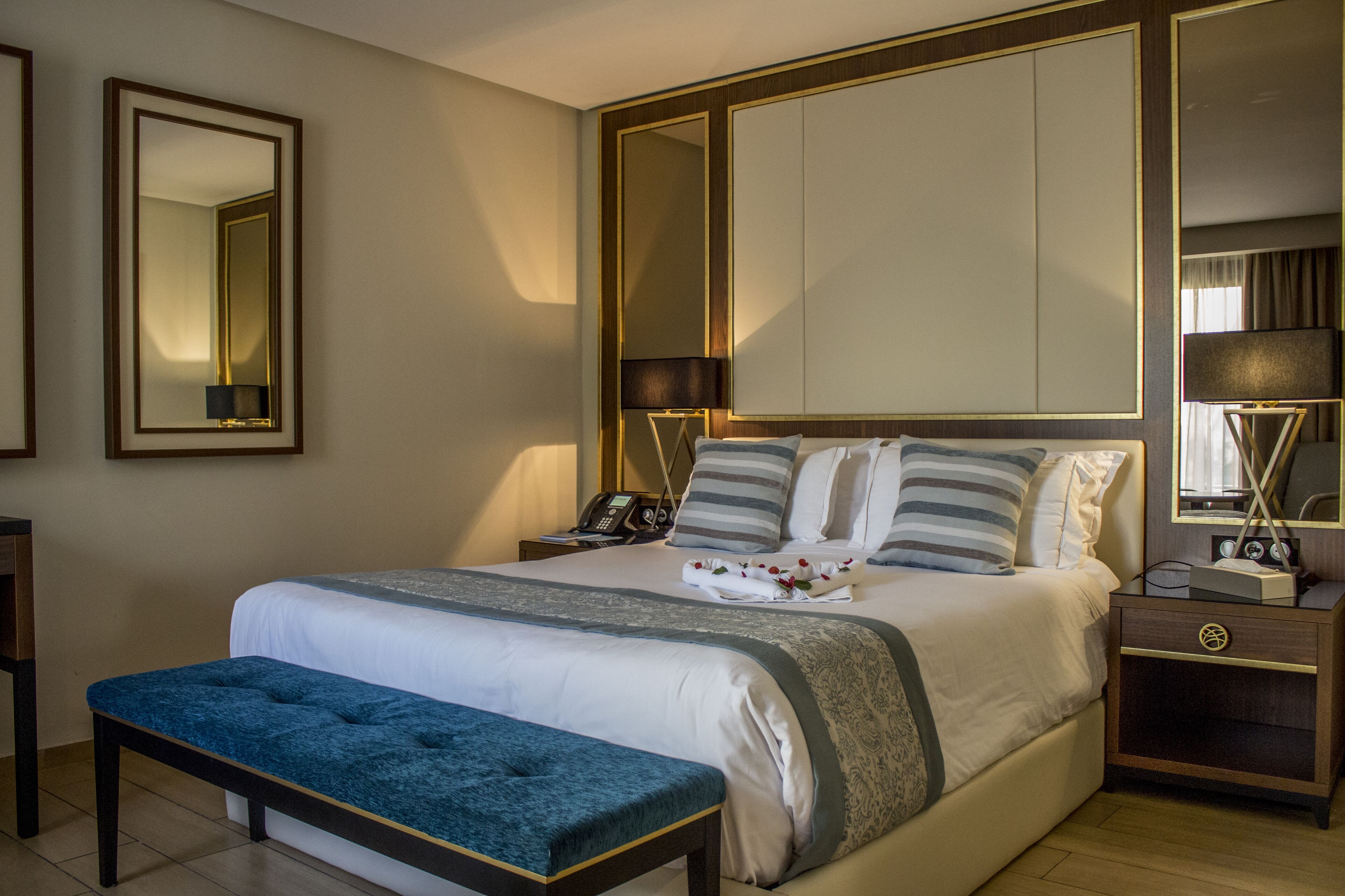 Una habitación de hotel con una cama grande, mesitas de noche, un banco y un armario.