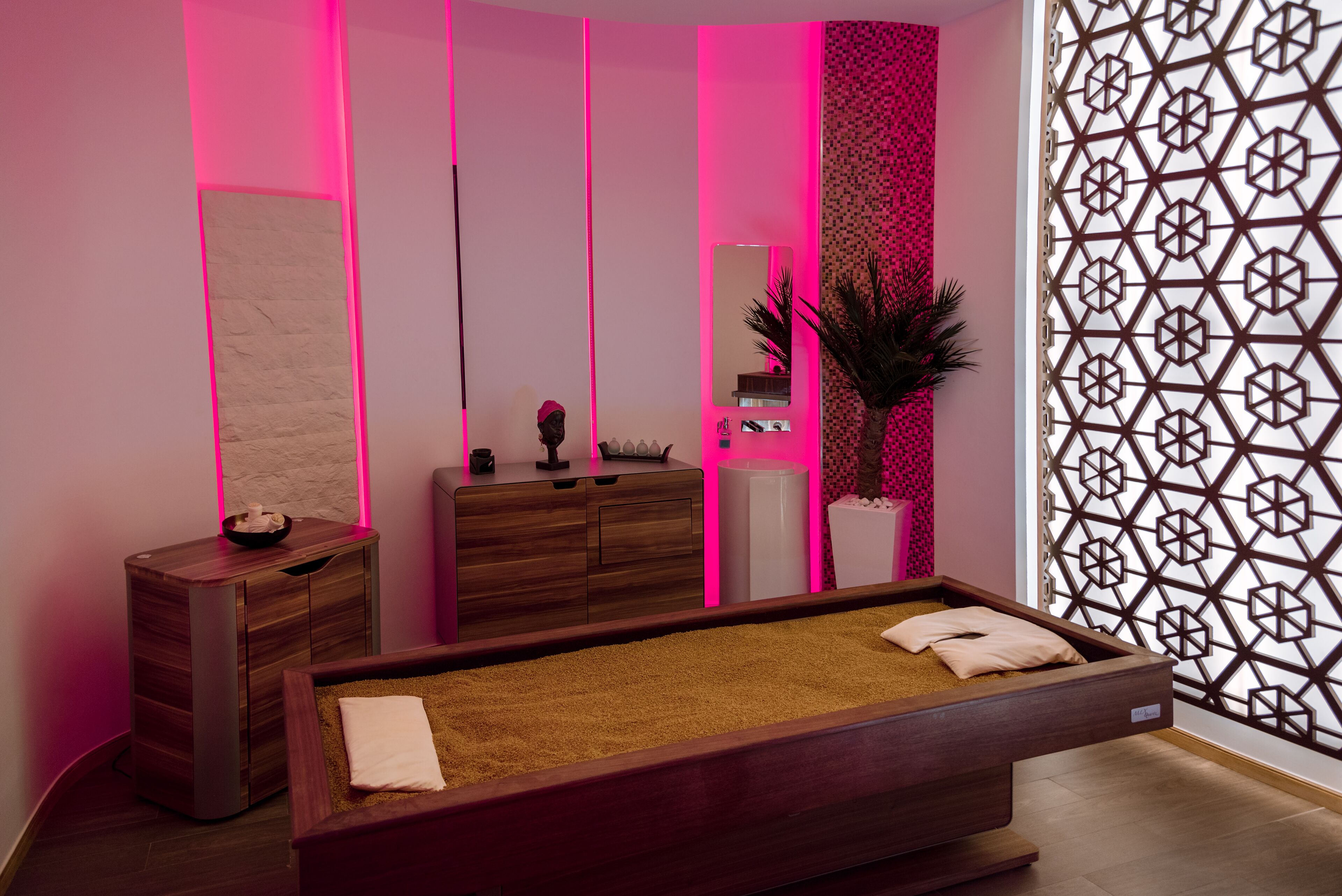 A modern spa room with a massage table, wooden cabinets, a mirror, and a decorative partition.