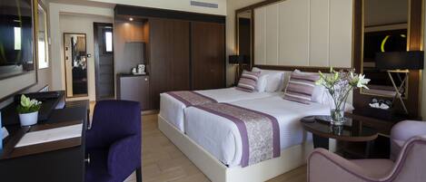 A hotel room with a large bed, a desk, a chair, a TV, and a wardrobe.