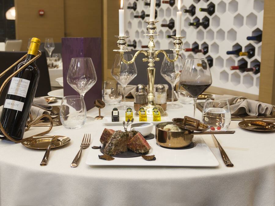 A dining table set with wine glasses, a bottle of Merlot, and a centerpiece of candles.