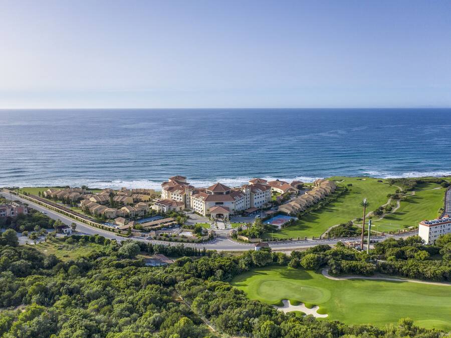 Un complejo turístico frente al mar con varias edificaciones, un campo de golf y vistas al océano.