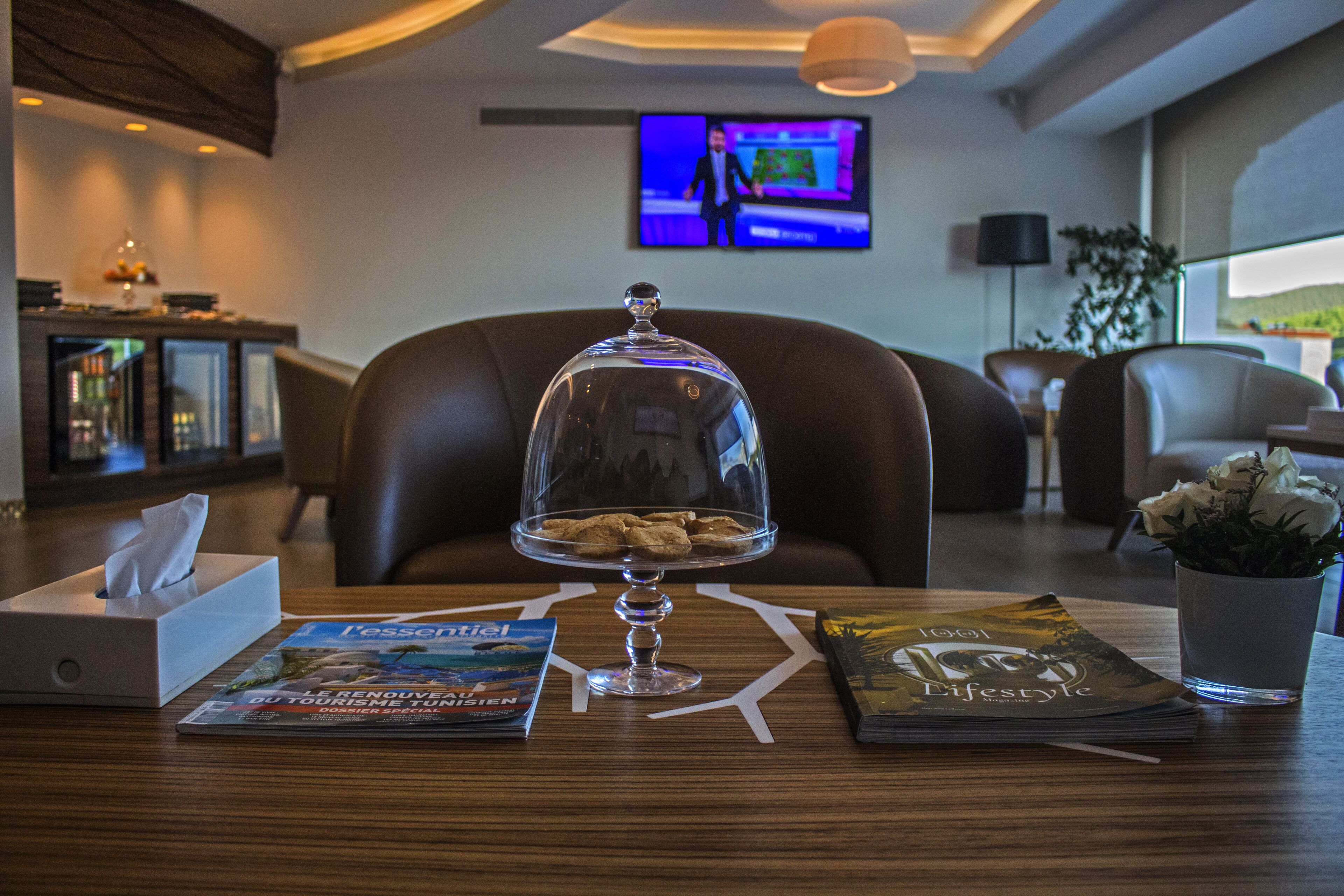 A hotel lobby with a wooden reception desk, a glass display case with cookies, magazines, and a tissue box.