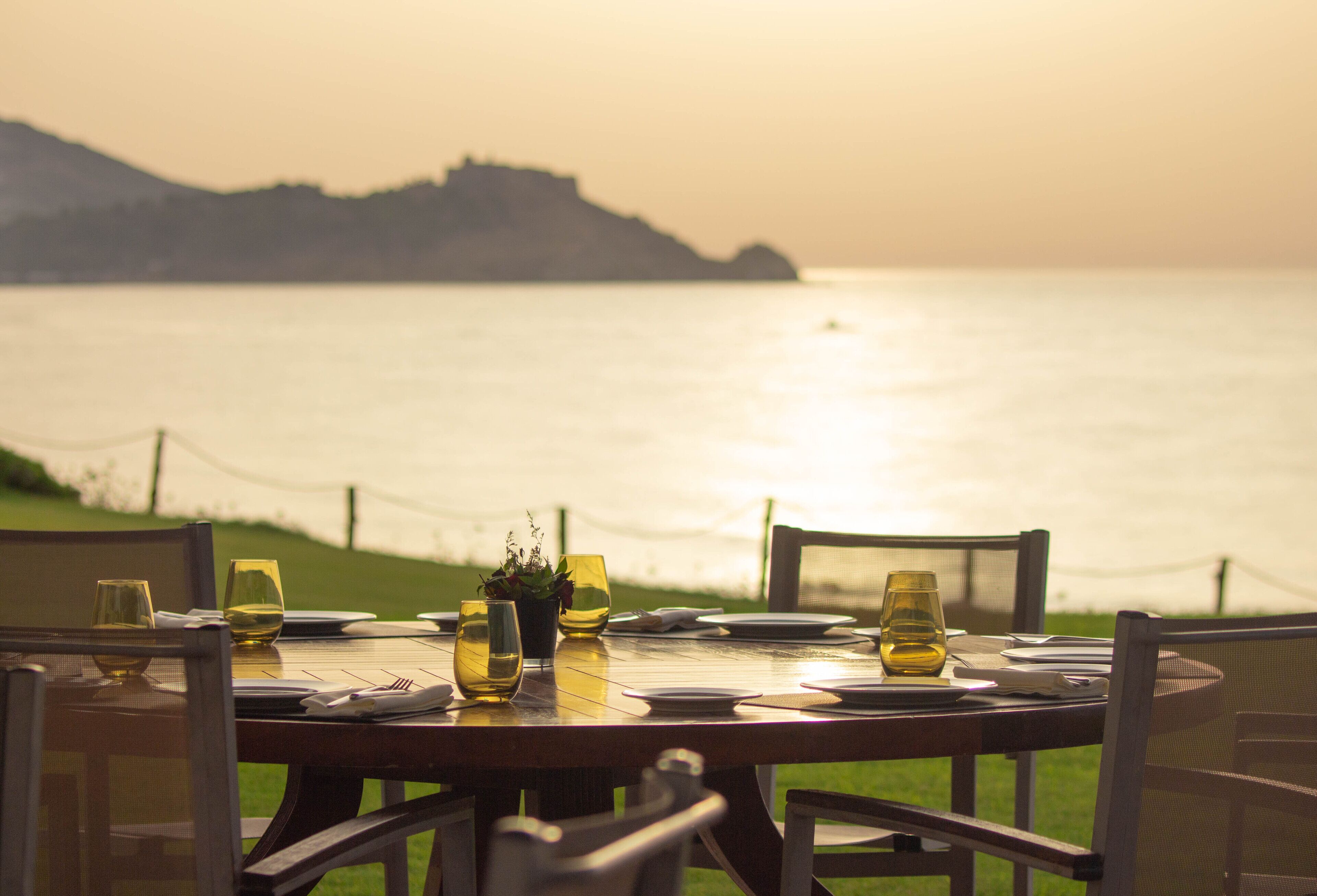 Une table dressée pour le dîner, avec vue sur la mer et le paysage lointain.