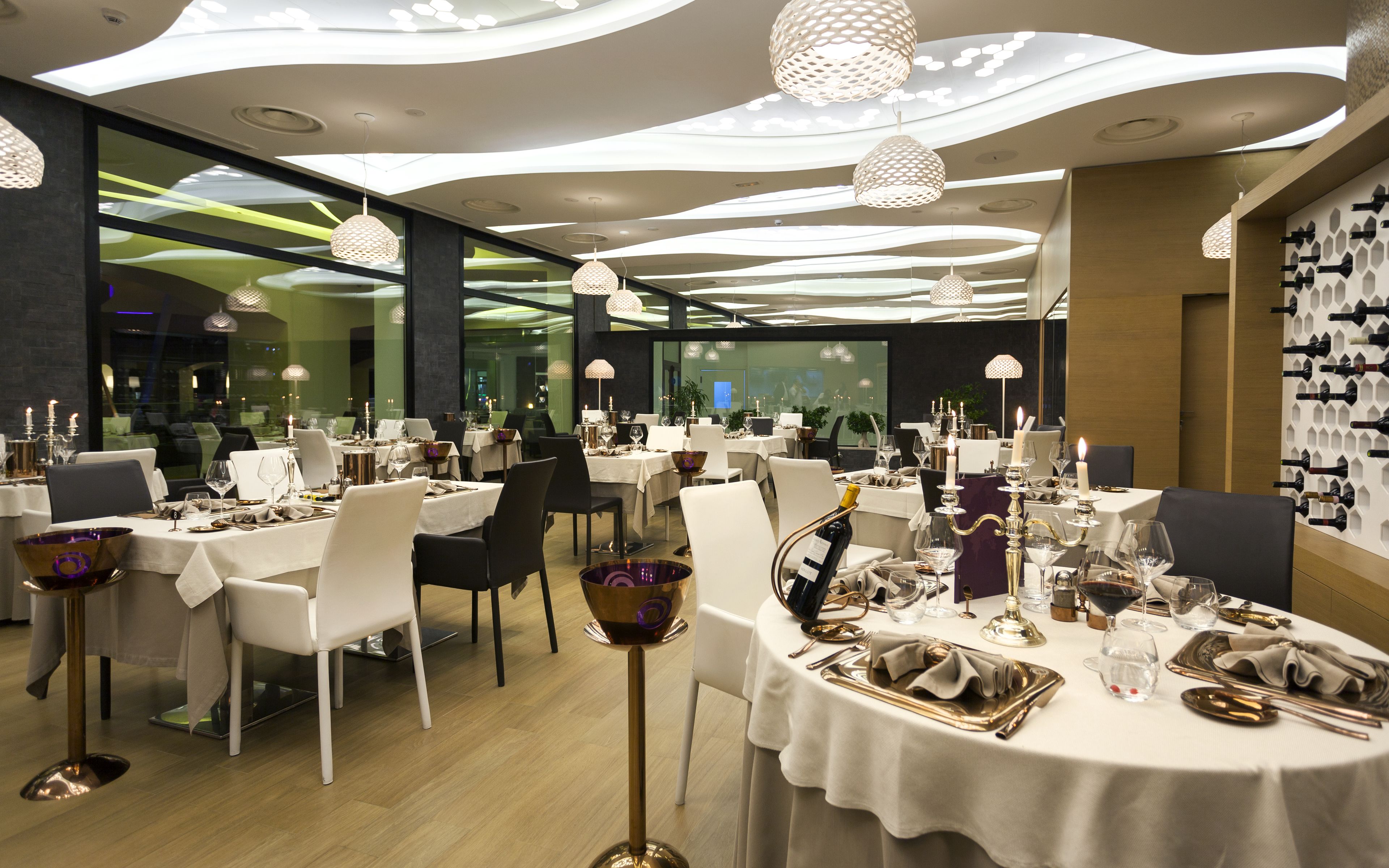 A modern restaurant with round tables, white tablecloths, and candle-lit centerpieces.