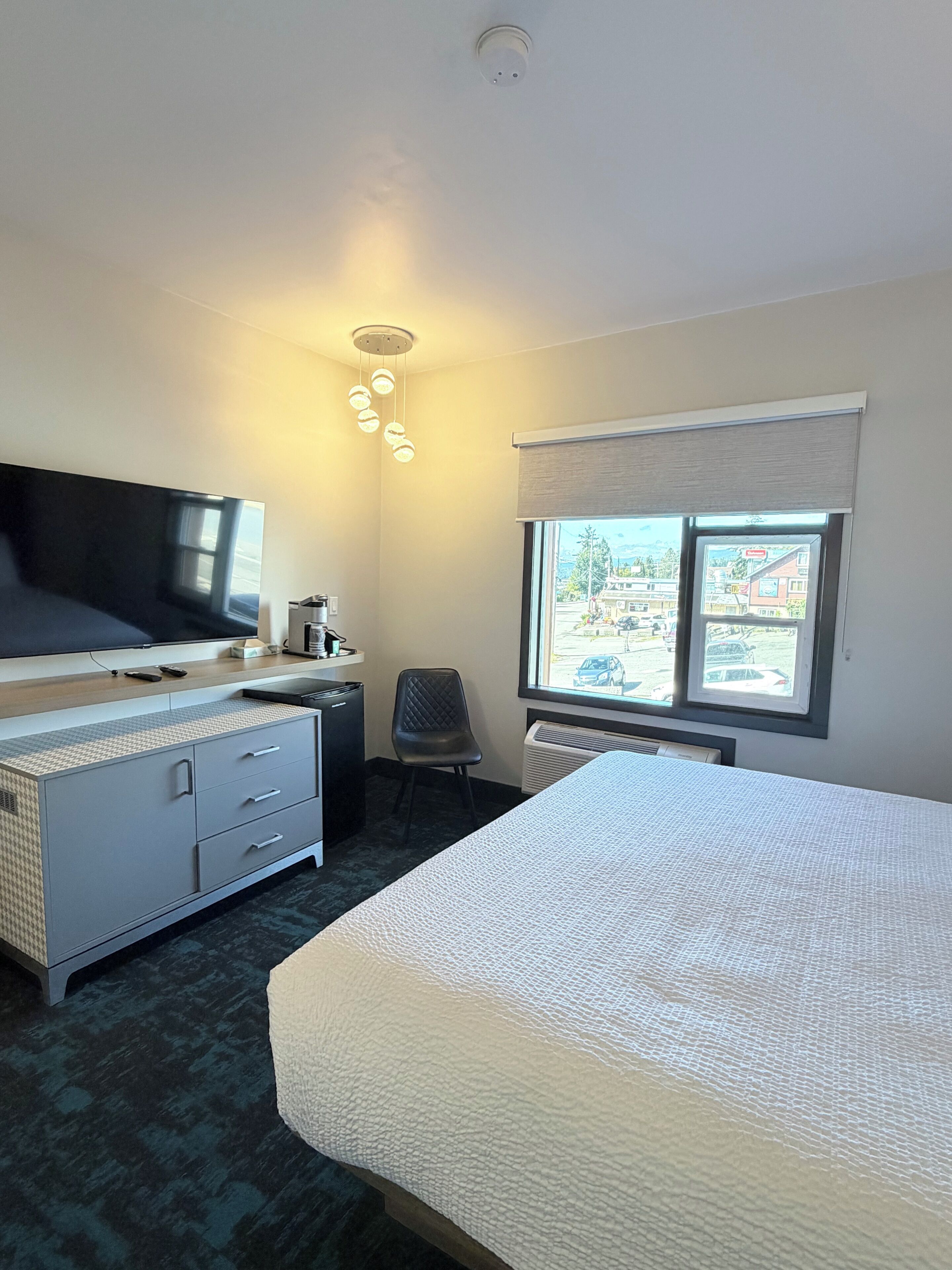 A hotel room with a bed, a desk, a chair, a television, and a window with a view of the outside.