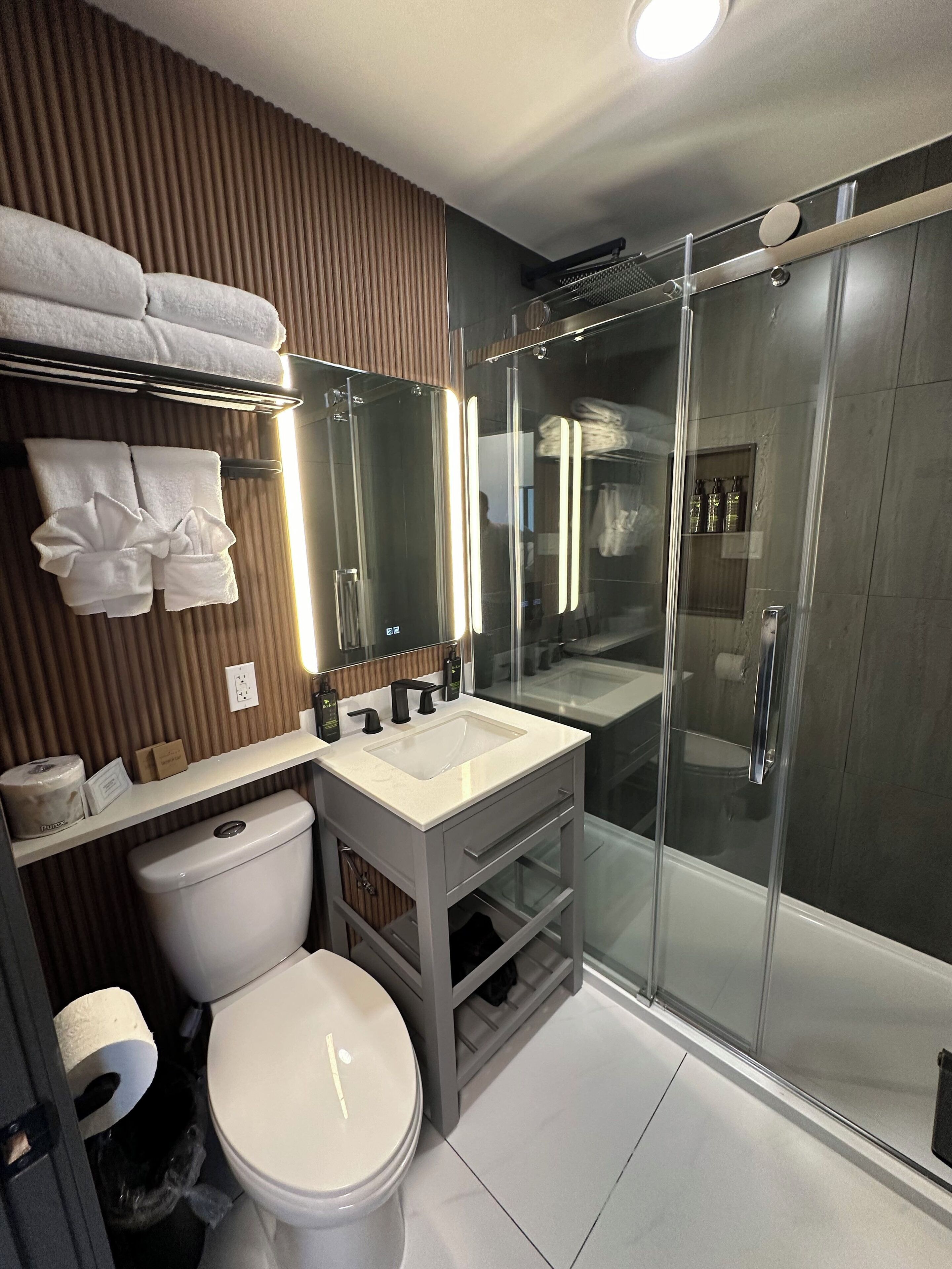 Un baño moderno con cabina de ducha de vidrio, inodoro blanco y tocador con espejo.