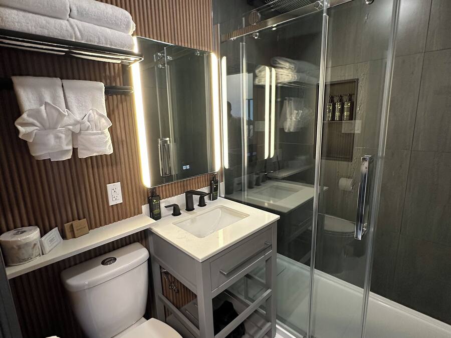 Un baño moderno con cabina de ducha de vidrio, inodoro blanco y tocador con espejo.