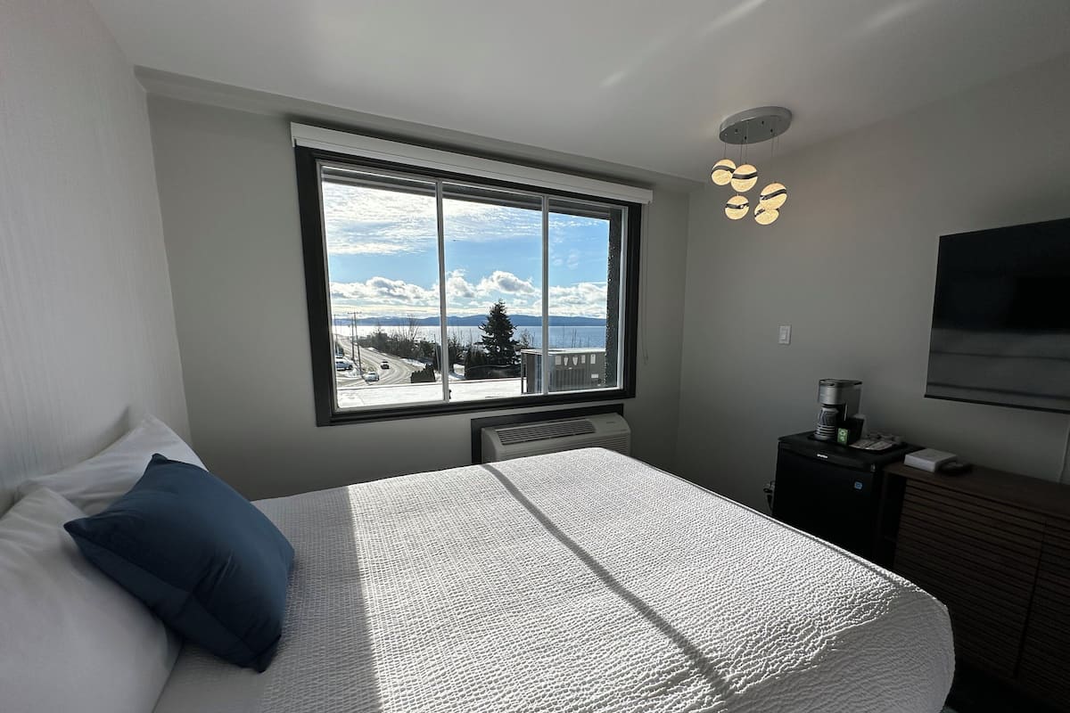 Un dormitorio con una cama grande, una ventana con vistas a una carretera y montañas, un calentador, una cafetera y un televisor en la pared.