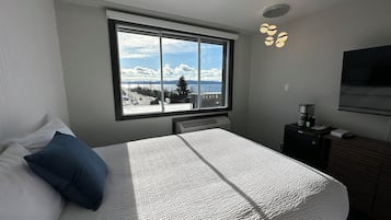 Un dormitorio con una cama grande, una ventana con vistas a una carretera y montañas, un calentador, una cafetera y un televisor en la pared.