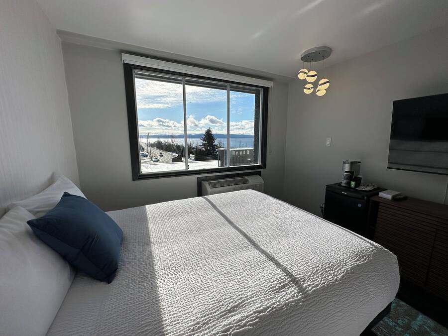 Un dormitorio con una cama grande, una ventana con vistas a una carretera y montañas, un calentador, una cafetera y un televisor en la pared.