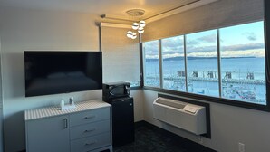 A modern hotel room with a large window, a flat-screen TV, a small kitchenette, and a ceiling light fixture. - Waterways, A Boutique Hotel (Powell River)