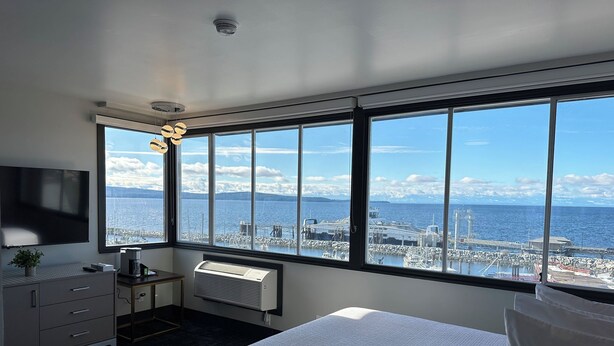 A hotel room with a large window offering a view of a harbor and mountains. - Waterways, A Boutique Hotel (Powell River)