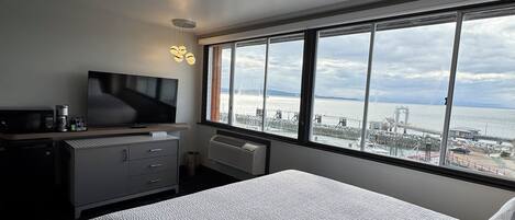 Camera d'hotel con un letto grande, una scrivania con televisore a schermo piatto, un termosifone e vista sul mare e su edifici industriali.