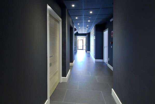 A corridor with dark walls, a light-colored floor, and recessed ceiling lights. - Hotel Villa Arce (Puente Viesgo)