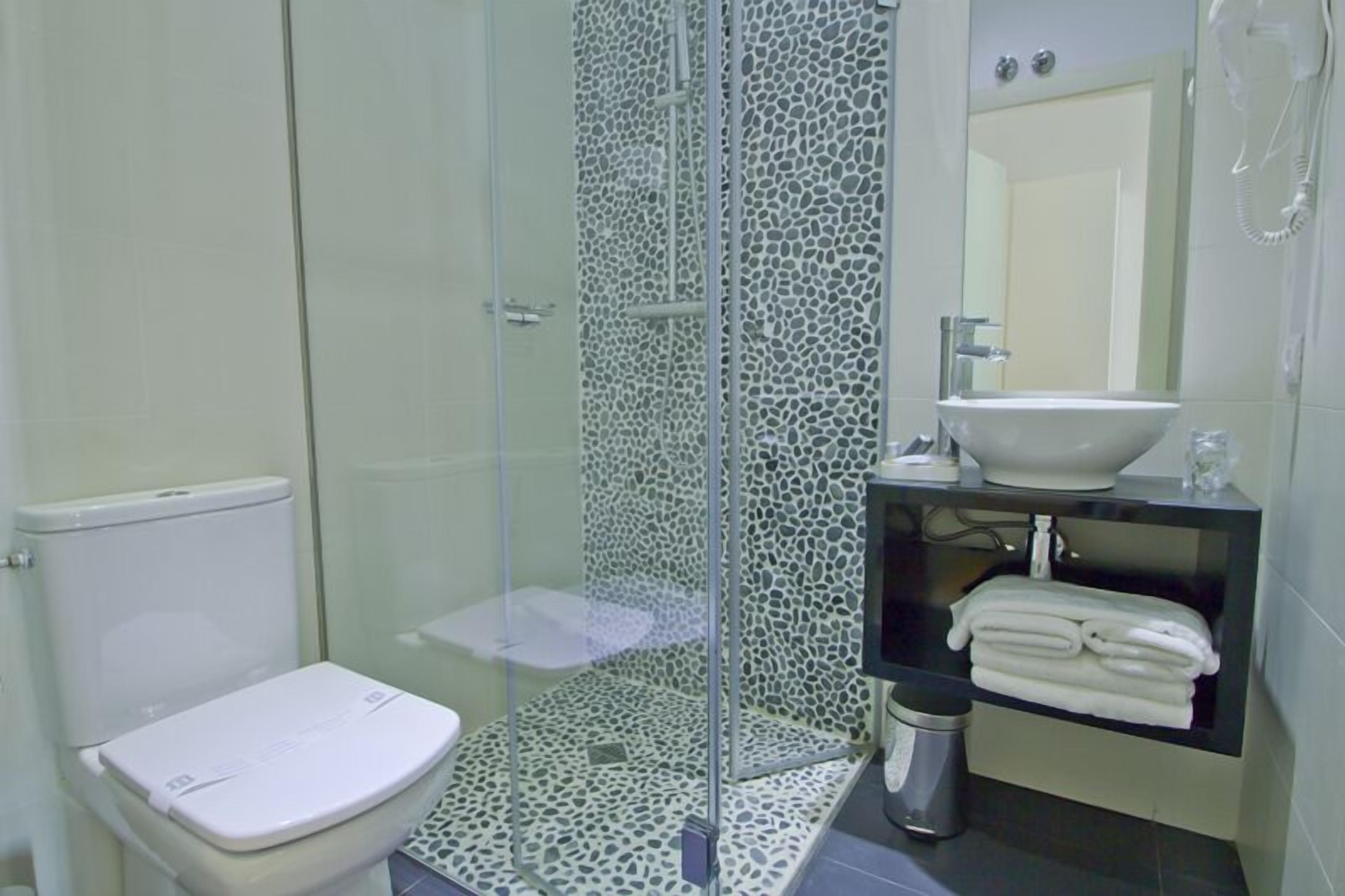 Un baño con ducha envuelta en vidrio, inodoro, lavamanos y un perchero para toallas.